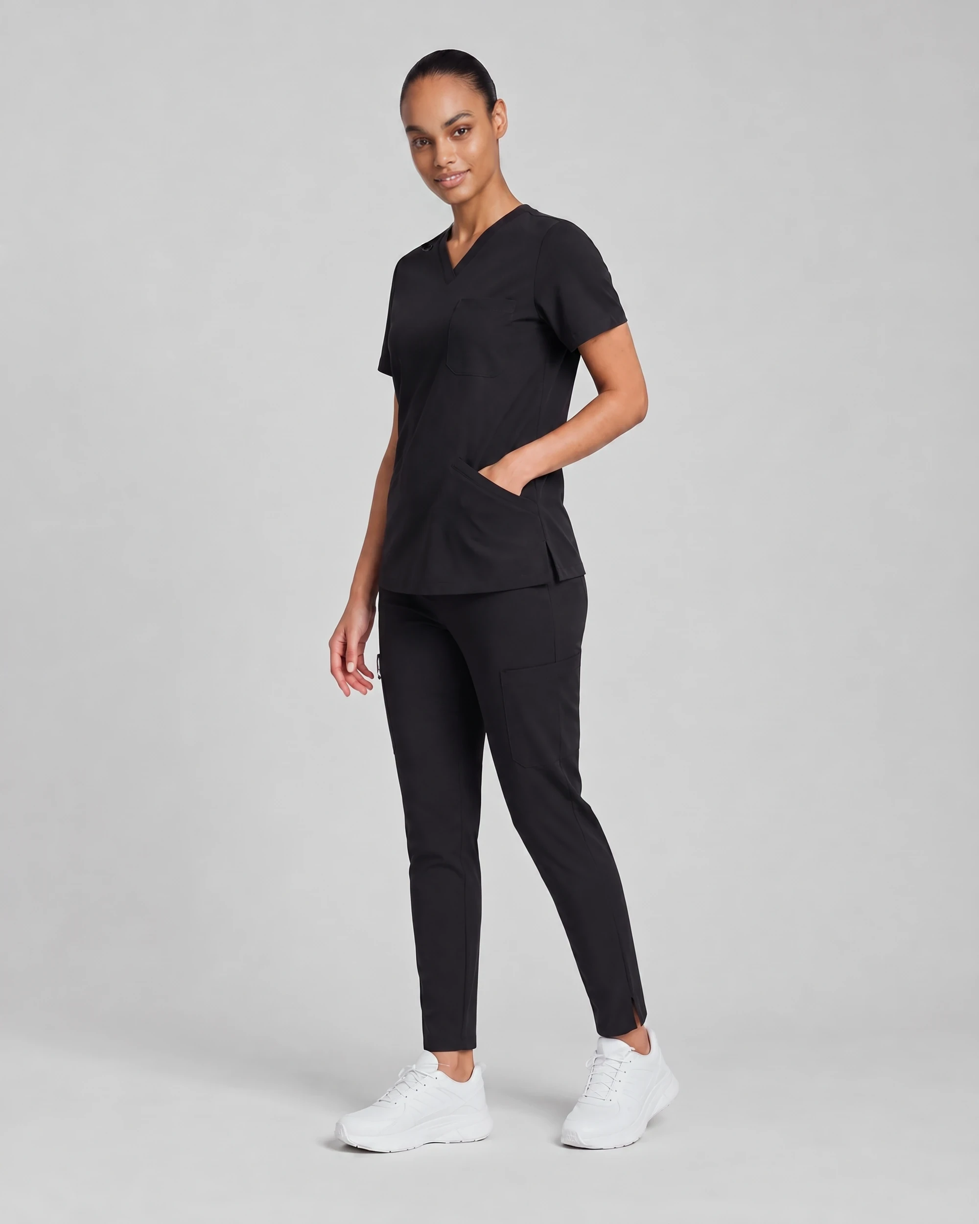 Woman wearing the Core Scrub Set in Black, three-quarter view showing the V-neck top and straight-leg pant