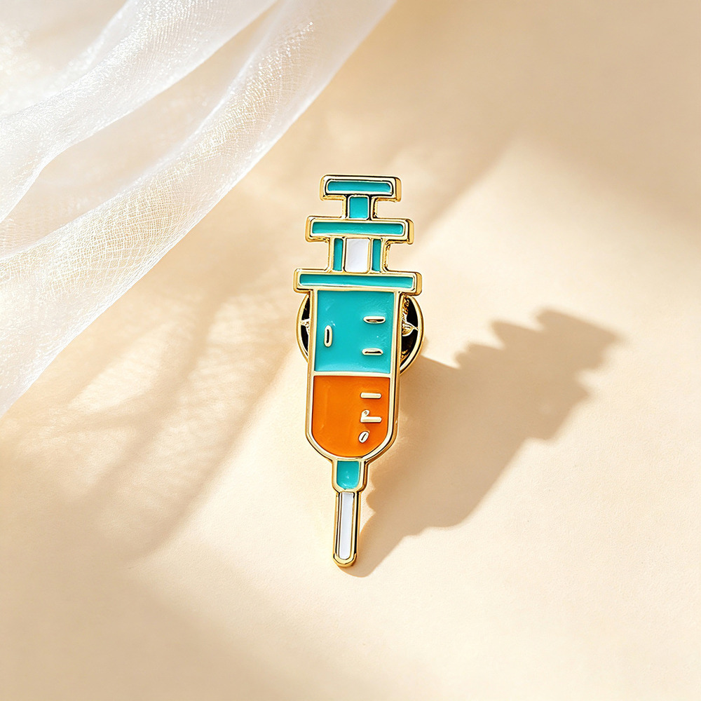 Teal and orange syringe enamel pin with a gold outline